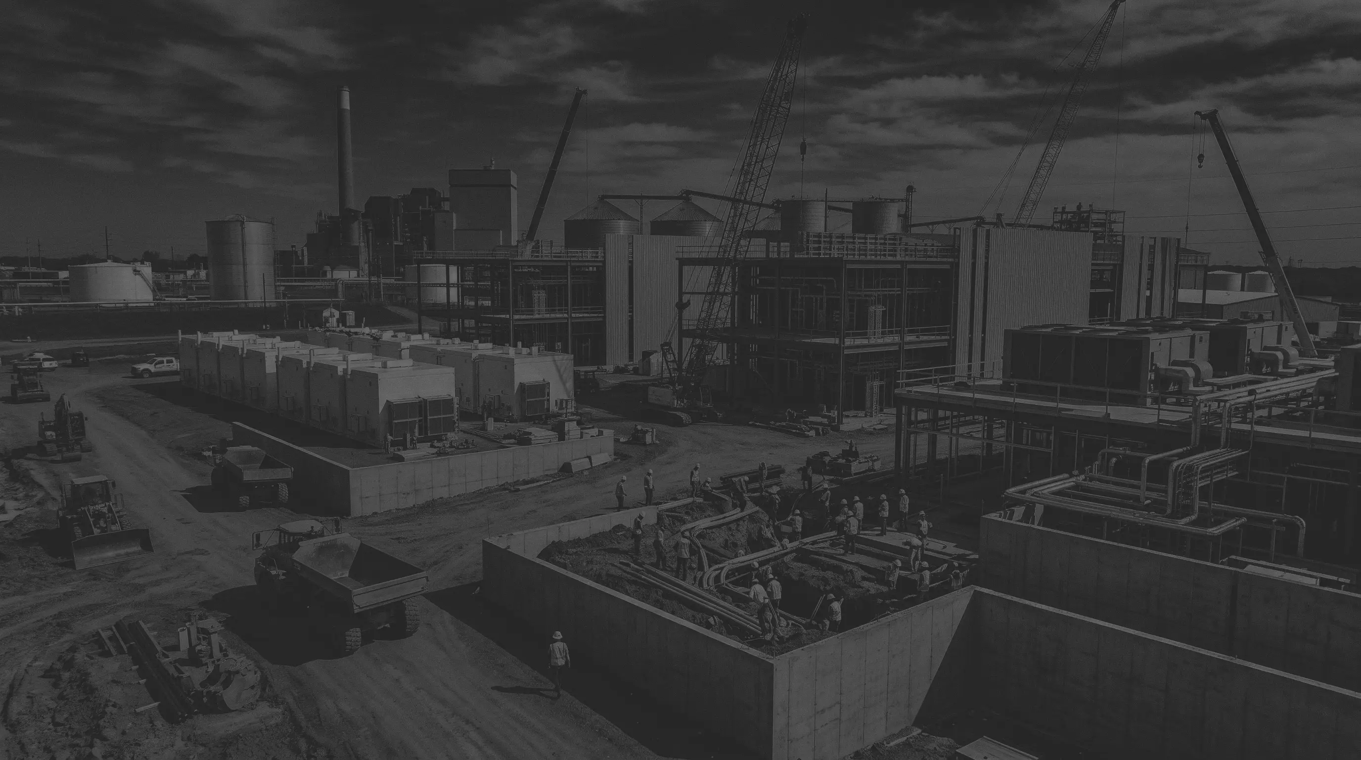 Black and white aerial photograph of a battery-storage and industrial plant construction site, with cranes, rows of modular units and pipework.